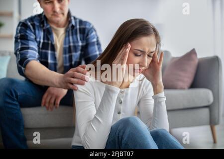 Frau mittleren Alters fühlt sich gestresst, steht vor gesundheitlichen Problemen, hat Probleme, ihr Mann unterstützt sie zu Hause Stockfoto