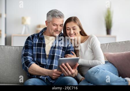 Reifes Ehepaar, das zu Hause auf der Couch sitzt und mit einem Tablet-pc zusammenarbeitet, Filme ansieht und aus der Ferne arbeitet Stockfoto