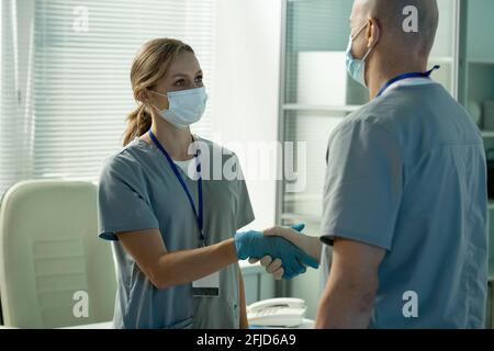 Attraktive junge Chirurg in Scrubs schüttelt die Hand des Kollegen in Büro während des Treffens mit ihm vor der Operation Stockfoto