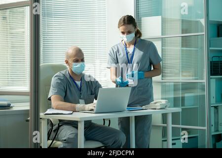 Seriöse Chirurgen in Scrubs mit Laptop während der Analyse Online-Medizin Tests im modernen Büro Stockfoto