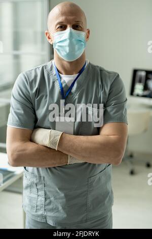 Porträt eines zufriedenen Glatzenchirurgen in Gesichtsmaske und Handschuhen Stehen mit gekreuzten Armen im modernen Büro Stockfoto