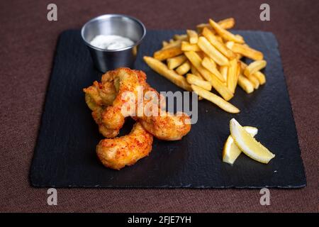 Fisch im Teig mit Sauce und Pommes auf einem schwarzen Teller. Stockfoto