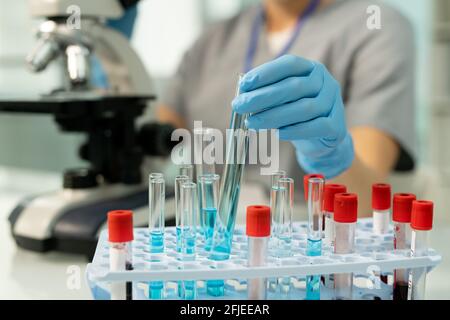 Nahaufnahme eines nicht erkennbaren medizinischen Forschers in Handschuhen, der das Reagenzglas einsetzte Der blauen Flüssigkeit in das Rack mit Blutproben Stockfoto