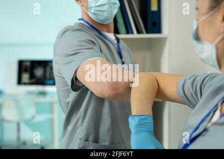 Nahaufnahme von freundlichen Chirurgen in Scrubs und Masken stehen Ärztekammer und Begrüßung einander mit Ellenbogenstoß Stockfoto