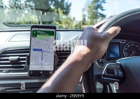 Google Maps App GPS auf Smartphone im Auto mit Blick auf Lenkrad und Hände des Fahrers Stockfoto