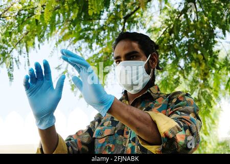 Ein junger indischer Mann, der eine medizinische Gesichtsmaske trägt Und Latexhandschuhe in einem Park Stockfoto