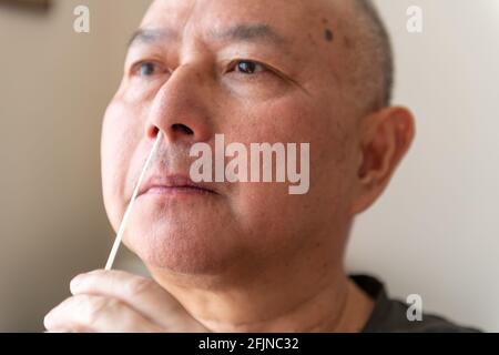 Ein gereifter asiatischer Mann, der eine Abstrichprobe nimmt und einen Covid-19-Selbstheimmesstest durchführt. Stockfoto
