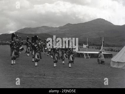 1956, historisch, eine schottische Pfeifenband, die bei den Greenock Highland Games in Schottland spielt. Erstmals in den 1820er Jahren in Invergarry dokumentiert, zeigten die Einheimischen bei den Spielen ihre Stärke und Beweglichkeit bei verschiedenen Aktivitäten wie dem Hammerwerfen, darunter auch schottisches Tanzen und Paspeln. Der Besuch von Königin Victoria auf dem Braemer-Treffen im Jahr 1848 begann die Royal Association und sah sie in der Popularität zu erhöhen. In den Sommermonaten finden in ganz Schottland verschiedene Veranstaltungen statt, die als Highland Games oder einfach nur Versammlungen bekannt sind. Stockfoto