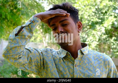 Ein Porträt eines jungen, müden indischen Mannes, der dasteht Ein Park mit der Hand auf dem Kopf Stockfoto