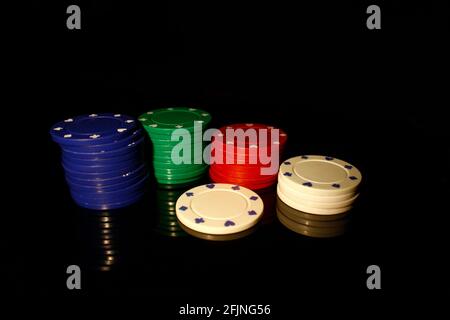 Vier Farben Casino-Chips stapeln mit einem weißen Chip vorne, isoliert auf schwarz mit Reflexion Stockfoto