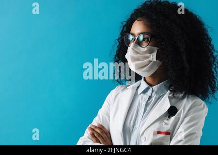 Selbstbewusste Ärztin mit Brille und Schutzmaske, die wegschaut Auf blauem Hintergrund Stockfoto