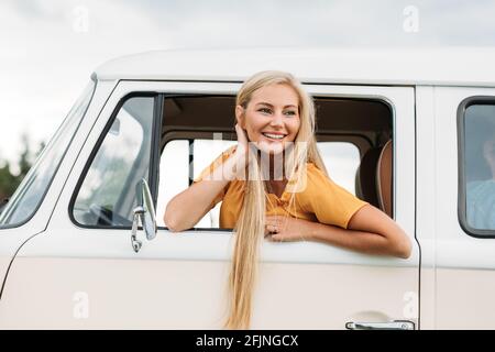 Glückliche Frau mit langen Haaren schaut aus dem Autofenster Während Sie auf dem Fahrersitz sitzen Stockfoto