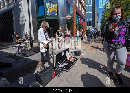 Menschen mit schützenden Gesichtsmasken passieren Live-Bands, die während der Coronavirus-Pandemie in der Oxford Street in London spielen. Stockfoto