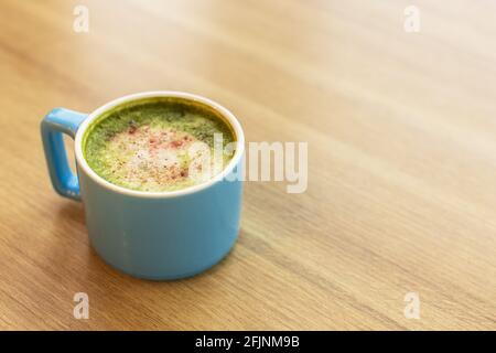 Blaue Tasse mit grünem Tee Matcha Latte, mit gefriergetrockneten Erdbeeren auf einem Holztisch, Platz zum Kopieren. Gesundes Ernährungskonzept, Getränke mit Gemüse o Stockfoto