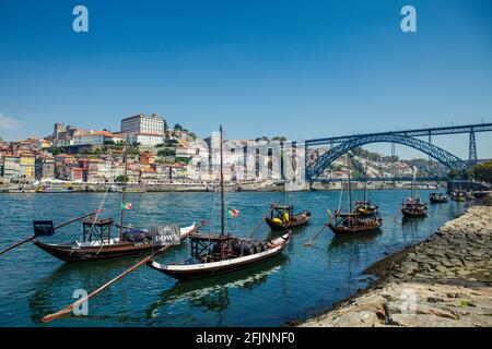 Schiffe auf dem Fluss Douro in der historischen Stadt Porto, mit der ikonischen Dom Luis Brücke im Hintergrund. Stockfoto