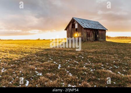 Alte Scheune auf Ackerland in Schweden, die immer wieder fällt Abgesehen von einem Sonnenuntergang, der während des ganzen Hauses ausstrahlt Der Monat April Stockfoto