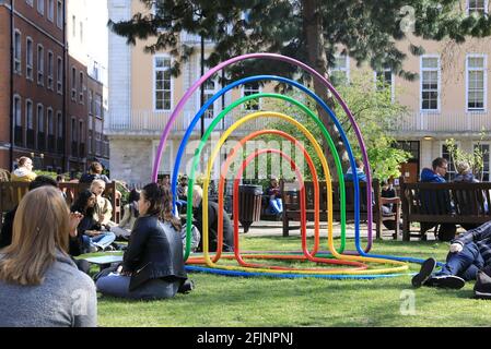 Menschen, die sich in der Frühlingssonne entspannen, durch die neue Regenbogen-Kunstinstallation Hello Sunshine von GrayGray im Soho Square im Zentrum von London, VEREINIGTES KÖNIGREICH Stockfoto