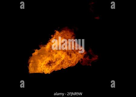 Ein Flammenstapel in der Nacht. Dies ist der Fackelstapel in einer Raffinerie. Alles, was sichtbar ist, ist die Flamme auf schwarzem Hintergrund. Vom Wind geblasene Flamme. Stockfoto