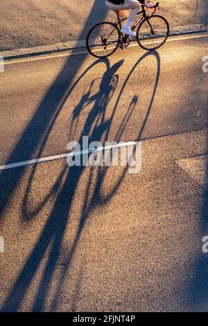 Ein Radfahrer wirft am späten Nachmittag einen langen Schatten Sonnenschein Stockfoto