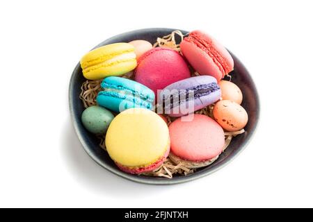 Bunte Makronen und Schokoladeneier in blauer Keramikschale isoliert auf weißem Hintergrund. Seitenansicht, Nahaufnahme, Stillleben. Frühstück, morgens, Konz Stockfoto