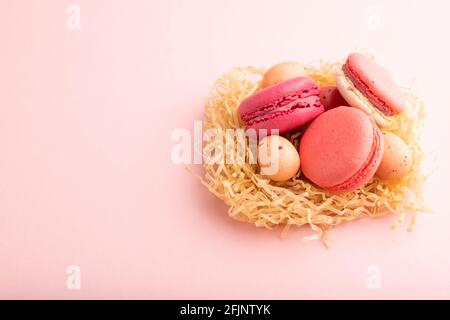 Lila und rosa Makronen und Schokoladeneier in dekorativem Papiernest auf rosa pastellfarbenem Hintergrund. Seitenansicht, Kopierraum, Stillleben. Frühstück, morgens Stockfoto