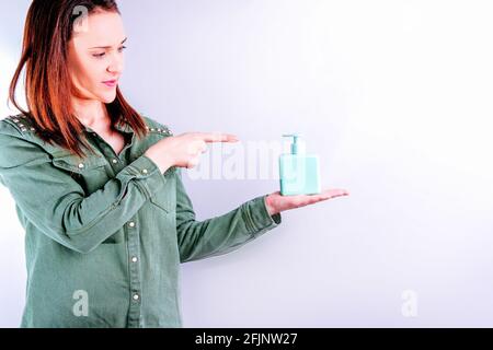 Schöne junge Erwachsene Frau zeigt einen Topf mit der Hand oder Körpercreme zeigt mit Platz für die Kopie auf weißem Hintergrund Stockfoto