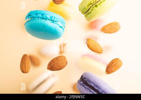 Bunte fliegende Makronen und in der Luft gefrorene Mandeln auf unscharfem beigen Hintergrund. Draufsicht, flach liegend, Nahaufnahme. Frühstück, Morgen, Konzept. Stockfoto