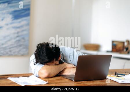 Müde hispanic, Manager, Freiberufler oder Student, der mit einem Laptop arbeitet oder studiert, Kopfschmerzen und Stress hat, auf dem Arm liegt, am Tisch einschläft, Ruhe braucht Stockfoto