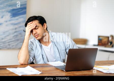 Müde abgestumpft gemischte Rasse hispanic Kerl, Mitarbeiter, Freiberufler oder Student, in Freizeitkleidung, arbeiten oder studieren am Laptop, erleben Stress bei der Arbeit, Kopfschmerzen, brauchen eine Pause, Augen geschlossen Stockfoto