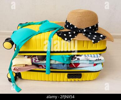 Set von Kleidung und Accessoires für Reisen auf dem Boden In einem gelben Koffer Stockfoto