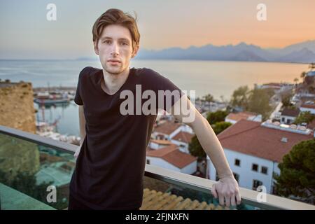 Die Altstadt von Antalya bei Sonnenuntergang und ein schlanker junger Europäer mit ernstem Gesicht stehen auf der Aussichtsplattform. Stockfoto