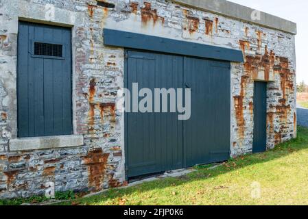 Eine hellblaue Vintage-Holztür mit einem kleinen Fenster, das sich oben öffnet. Der Eingang ist in einer alten rustikalen strukturierten Felswand. Stockfoto