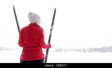 Frau in roter Winterjacke stehend und mit Skiern auf dem schneebedeckten Berg. Hochwertige Fotos Stockfoto