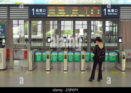 Eine alleinstehende Frau wartet auf ihren Zug in Jiaxing, China, und kann dann ihren Personalausweis scannen, um durch die Drehkreuze zum Bahnsteig zu gelangen. Stockfoto