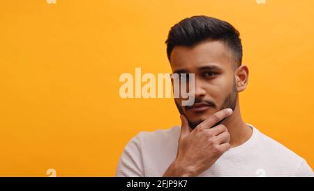 Porträt eines hübschen erwachsenen Mannes, der sein Kinn berührt und nach oben schaut. Gemischtes männliches Modell mit moderner Quiff-Frisur vor orangefarbenem Hintergrund. Hochwertige Fotos Stockfoto