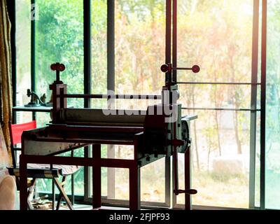 Ätzpresse, Kunstausstattung für die Druckgrafik. Alte rote Radierpresse im Kunststudio in der Nähe einer Glasschiebetür auf dem grünen Gartenhintergrund außerhalb des b Stockfoto