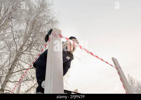 Ein Installateure in einem Hut mit Ohrenklappen montiert den Rahmen Von einem Schlitten aus Holzbalken Stockfoto