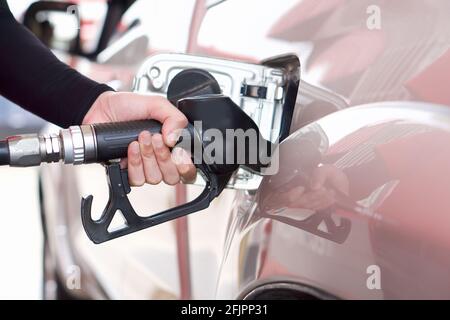 Tankstellenmitarbeiter mit schwarzer Armhülle für Sonnenschutzmittel, die den Bronze-Pickup-LKW-Tank füllt. Nahaufnahme Hand mit schwarzer Gaspumpendüse. Stockfoto