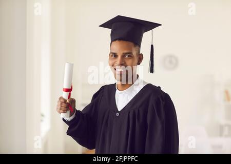 Afroamerikanische Studentin in schwarzem akademischen Kleid und Mütze mit Diplom Und lächelnd Stockfoto
