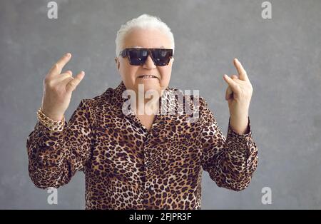 Ein steiler reifer Mann zeigt ein Felsschild mit beiden Händen auf grauem Hintergrund. Stockfoto