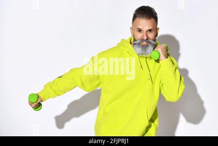 Glücklich lächelnd alten brutalen bärtigen Mann in gelben Hoodie genießt Fitnesstraining mit grünen Kurzhanteln in den Händen Stockfoto