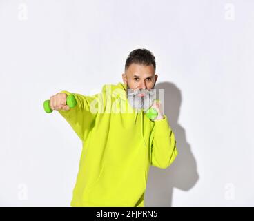 Glücklich aktiven alten brutalen bärtigen Mann in gelben Hoodie genießt Fitness-Training Boxen mit grünen Hanteln in den Händen Stockfoto