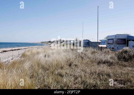 Fehmarn, Deutschland. April 2021. Wohnwagen stehen auf einem Campingplatz vor Dünen und Strand direkt an der Ostsee. Hotels und Pensionen sind geschlossen, auch mit dem Wohnmobil ist Urlaub kaum möglich. Glücklich, wer ein dauerhafter Camper in der Corona-Pandemie ist. Quelle: Frank Molter/dpa/Alamy Live News Stockfoto