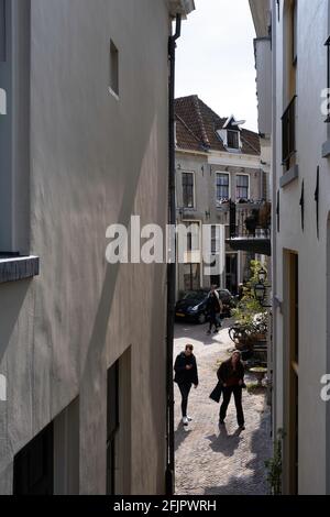 Das junge Paar geht zu einer schmalen Gasse, die zum Bergkerk in Deventer führt. Sie schaut auf die Kirche, er schaut auf sein Telefon Stockfoto