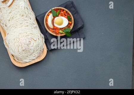 Ideyappam oder Noolappam, südindisches Frühstücksartikel aus rohem Reis Die in einer hölzernen Servierunterlage mit Ei angeordnet ist masala als gute Kombination Stockfoto