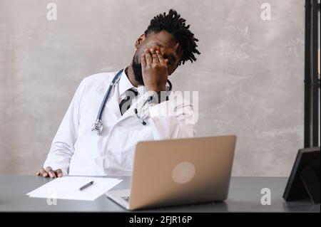 Lustig gelangweilt bei der Arbeit afroamerikanischen Arzt Arbeitnehmer Einschlafen am Schreibtisch, Mitarbeiter schlafen am Arbeitsplatz in der Nähe von Laptop Gefühl überarbeiteter Konzept Stockfoto