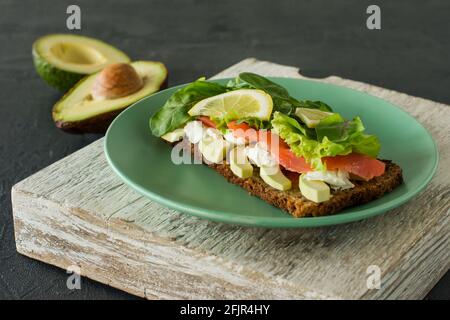 Sandwich mit geräuchertem Lachs-Weichkäse, Gitter und Avocado. Konzept für eine leckere und gesunde Mahlzeit. Essen auf einem Teller Stockfoto