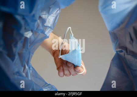 Die Hand wirft die medizinische Maske in den Müll. Ein Mann hält die unbrauchbare Gesichtsschutzmaske über einem Abfalleimer in der Halle. Ansicht von unten. Stockfoto