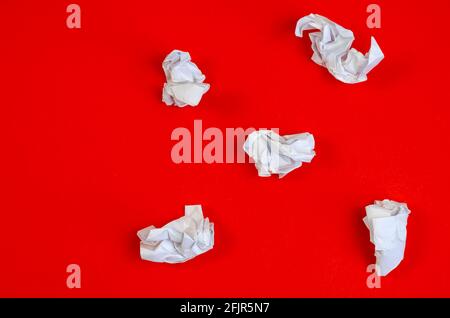 Zerknitterte Reste weißen Papiers auf rotem Hintergrund. Fünf zerknitterte Papierstücke liegen chaotisch. Draufsicht, flach liegend. Stockfoto