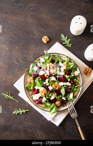 Rüben- oder Rote Beete-Salat mit frischer Rucola, Weichkäse und Walnüssen auf dem Teller, Dressing und Gewürzen auf dunklem Holzhintergrund, Kopierraum, Draufsicht/ Stockfoto